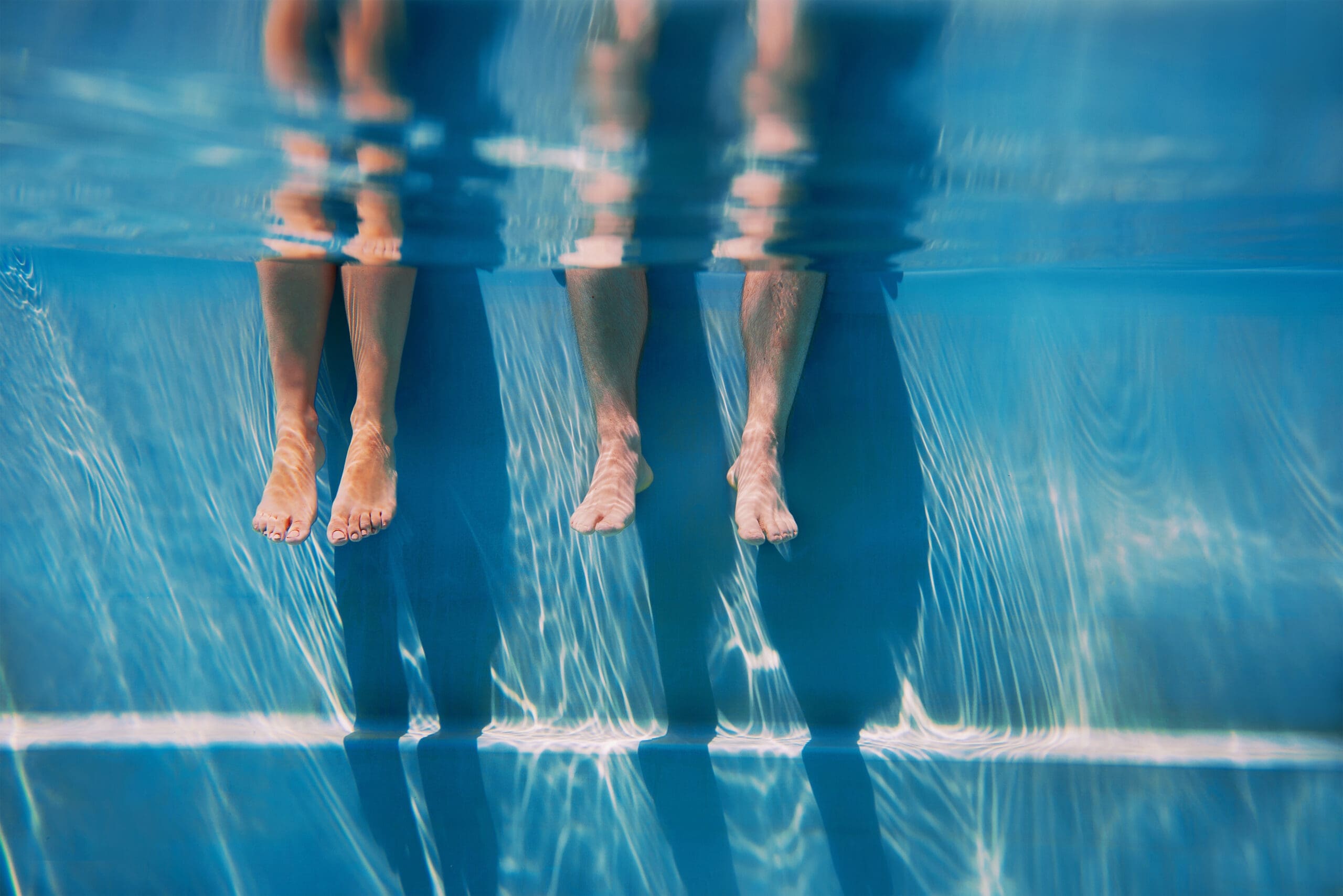 adults legs in sunny day in the swimming pool underwater